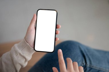 Kapalı mekanda oturan, akıllı telefonunu kullanan, ekranda dokunan bir kadının yakın plan görüntüsü. Bir kadının elinde beyaz ekran akıllı telefon modeli var. mesaj, mesajlaşma, sosyal medya, bağlantı, mobil uygulamalar