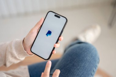 Chiang Mai, Tayland - Ekim 04 2023: Bir kadın evde oturuyor ve Iphone14 aracılığıyla PayPal uygulaması kullanıyor. Iphone14 ekranında PayPal logosu.