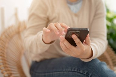 Minimalist bir kafede rahatlarken akıllı telefonunu arkadaşlarıyla sohbet etmek için kullanan sıradan giyinmiş bir kadının görüntüsü. İnsanlar ve teknoloji kavramları