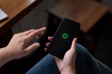 Chiang Mai, Tayland - Ekim 05 2023: Bir kadın evde oturuyor ve Iphone14 aracılığıyla Spotify uygulaması kullanıyor. Bir Iphone14 ekranında Spotify logosu.