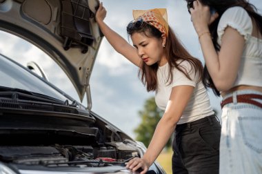 Kafası karışık ve stresli genç bir Asyalı kadın, arkadaşı motorları kontrol ederken, yardım beklerken, araba bozulduğunda araba sigortasını ya da teknik destek merkezini arıyor..