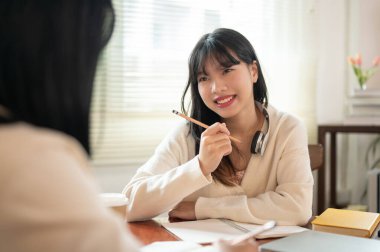 Güzel ve neşeli genç bir Asyalı kız üniversite öğrencisi arkadaşına matematik ödevinde yardım ediyor ya da hafta sonları kafede ödev yapıyor..