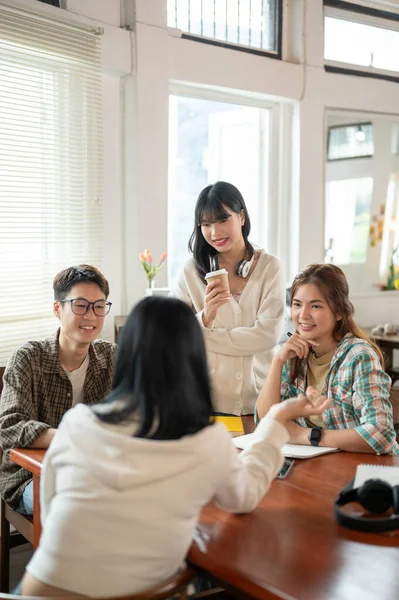 A group of creative and smart young Asian students are discussing work, sharing their ideas for a project, and having a meeting at a co-working space cafe. Teamwork, friendship, co-working, startups