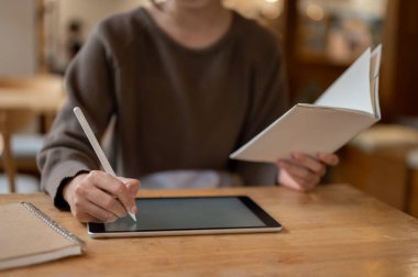 Not alan, dijital tableti üzerinde çalışan, kahve dükkanında uzaktan çalışan bir kadının kırpılmış görüntüsü. Öğrenci, serbest çalışan, iş kadını.