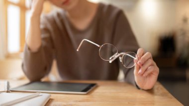 Stresli ve yorgun bir kadın gözlüğünü çıkarıyor, baş ağrısı çekiyor ve hafta sonları bir kafede çalışırken kendini çok yorgun hissediyor. yakın plan resim