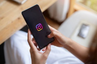 Chiang Mai, Tayland - 12 Ekim 2023: Bir kadın bir kafede dinlenirken akıllı telefonunda Instagram kullanıyor. iPhone 14 'te Instagram logosu. Sosyal medya platformu kavramı
