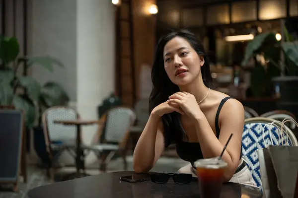 A gorgeous and confident young Asian woman in trendy clothes is sitting in a beautiful cafe or restaurant in the city, enjoying her weekend in the city. City girl, Urban lifestyle, leisure