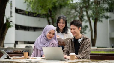 Bir grup genç üniversite öğrencisi proje detaylarını tartışıyorlar, dizüstü bilgisayar kullanıyorlar ve kampüs parkındaki bir masada grup projesi üzerinde çalışıyorlar. Eğitim kavramı