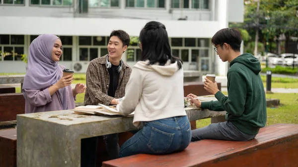 A group of diverse young college students is discussing and working on a group project at a table in a campus park together. Education concept