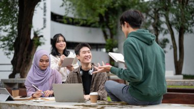 Yeşil kapüşonlu zeki ve neşeli bir Asyalı erkek üniversite öğrencisi arkadaşlarına matematik, özel ders ve arkadaşlarıyla birlikte kampüs parkında sınava hazırlanmalarında yardım ediyor. Eğitim kavramı