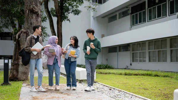 A group of cheerful, diverse Asian university students are enjoying talking and sharing their ideas while walking down the footpath in the campus park together. University life concept