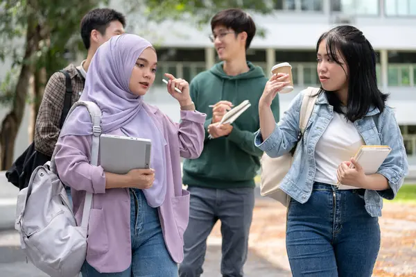 A group of diverse Asian university students are talking and sharing their ideas while walking down the footpath in the campus park together. University life and friendship concepts
