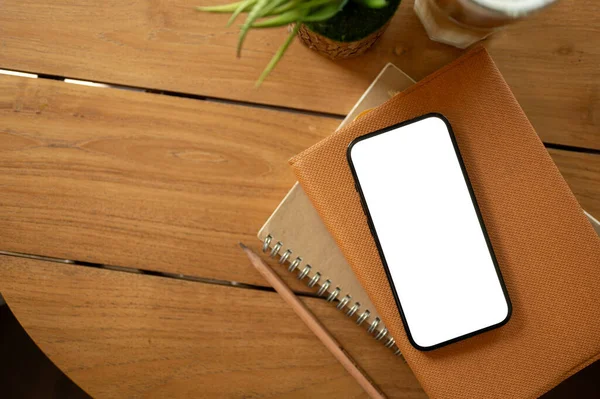 A white-screen smartphone mockup on a book on a wooden table. study table, office desk, minimal workspace top view image