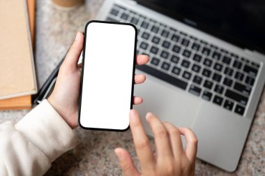 Modern masasında bilgisayarını ve aksesuarlarını kullanan bir kadının yakın plan görüntüsü. Grafik reklamlarınızı göstermek için beyaz ekran akıllı telefon. İnsanlar ve teknoloji kavramları