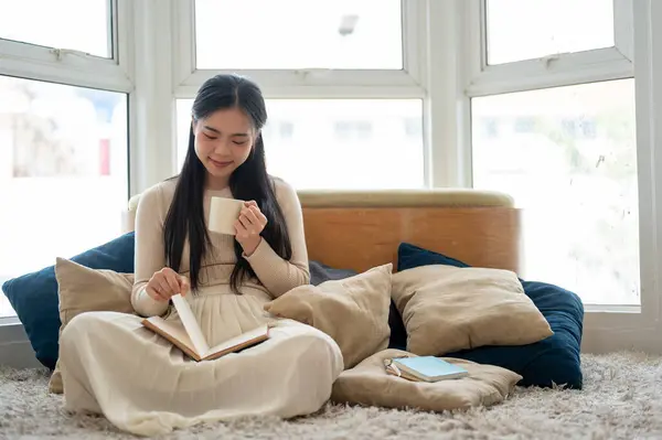 一位迷人而快乐的年轻亚洲女人一边在客厅看书一边喝咖啡 家庭生活方式和休闲概念 — 图库照片