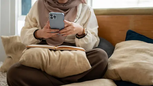 stock image Cropped image of an Asian-Muslim woman using her smartphone while relaxing in a living room. chatting, responding to messages, online shopping, updating her social media