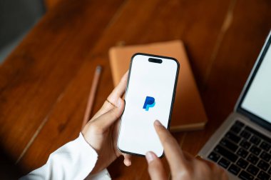 Chiang Mai, Tayland - 24 Ekim 2023: Masasındaki Iphone14 'e parasını aktarmak için Paypal kullanan bir kadın. Iphone14 ekranında Paypal logosu.