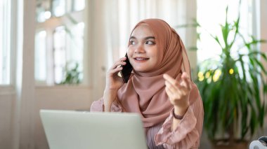 Çekici ve neşeli genç bir Asyalı-Müslüman kadın bir kafede uzaktan çalışırken birini arıyor ya da biriyle telefonla konuşuyor. İnsanlar ve teknoloji kavramları