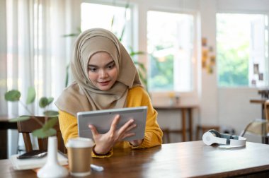 Çekici ve mutlu bir Asyalı-Müslüman kadın bir kafede dinlenirken dijital tablet kullanıyor. İnsanlar ve kablosuz teknoloji kavramları