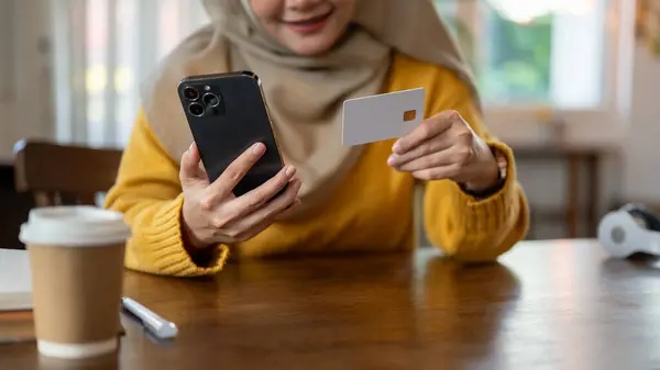Cropped image of a happy Asian-Muslim woman using her mobile banking application to pay her online bills or registering her credit card with an online shopping platform. Financial and lifestyle