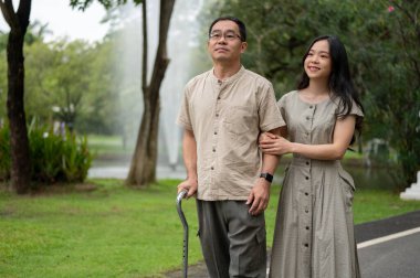 Güzel ve mutlu bir Asyalı genç kız kıdemli babasıyla parkta yürüyor, sabahları parkta birlikte gezmekten zevk alıyor. Aile, kız ve baba, bastonlu Asyalı bir baba.