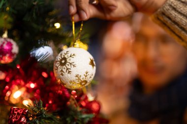 Çok güzel bir Noel süsü tutan bir adamın yakın plan resmi. Oturma odasındaki bir Noel ağacına Noel balosu süsü asıyor..