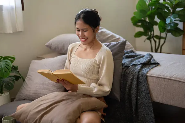 一位美丽而快乐的年轻亚洲女人正坐在床边的地板上 享受看书的乐趣 休闲和家庭生活概念 — 图库照片