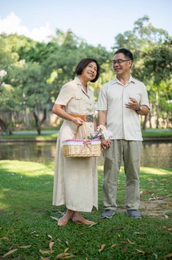 Mutlu Asyalı yaşlı çiftler, yaz günü yeşil parkta dolaşırken ve birlikte vakit geçirirken konuşmaktan zevk alıyorlar. Mutlu evlilik hayatı, sevgili emekli çift.