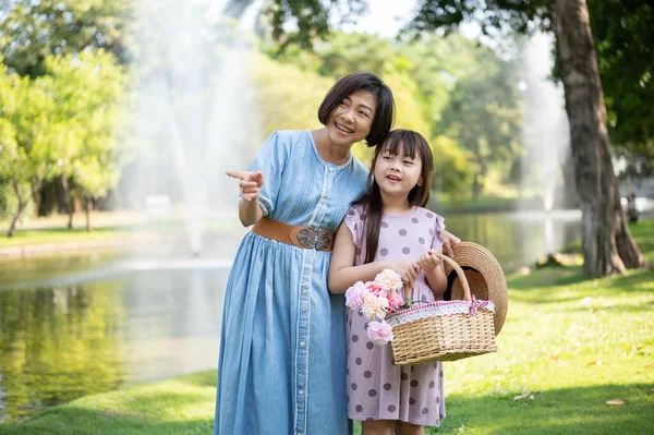 A happy and kind Asian grandmother is walking and having fun in the green park with her lovely granddaughter on the weekend. Leisure and family bonding concept