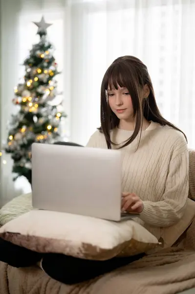 A beautiful Caucasian woman is working on her laptop on a couch in her beautiful living room on Christmas. Special holiday, people and technology concepts