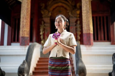 Geleneksel Tayland-Kuzey elbisesi giymiş genç ve güzel bir Tayland 'lı kadın elinde bir çelenkle tapınakta dua pozisyonunda duruyor. Saygı göster, değerlendir, bir dilek tut, Budizm