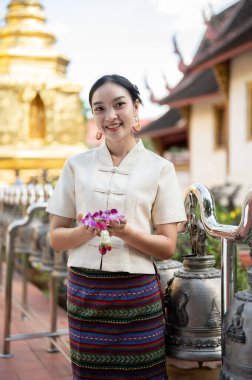 Tayland asıllı güzel ve gülümseyen bir kadının portresi. Geleneksel Tayland-Kuzey elbisesi içinde elinde bir çelenkle tapınakta duruyor. Tayland kültürü, Budist, Buda 'ya saygı gösterin.