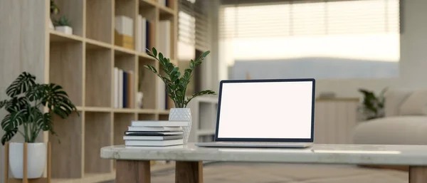 A white-screen laptop mockup, books, and a ceramic vase on a coffee table in a modern, minimalist home living room. 3d render, 3d illustration