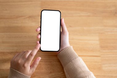 Tahta bir masada akıllı telefonunu kullanan bir kadının en iyi görüntüsü. Grafik reklamlarınızı göstermek için beyaz ekran akıllı telefon modeli. İnsanlar ve teknoloji kavramları