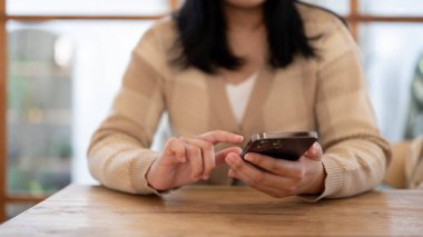 Kapalı bir masada otururken akıllı telefonunu kullanan bir kadın. Ekrana dokunmak, mobil uygulama kullanmak, mesajlaşmak, sosyal medyada kaydırmak. İnsanlar ve teknoloji kavramları
