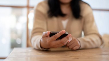 Kapalı bir masada otururken akıllı telefonunu kullanan bir kadın. Ekrana dokunmak, mobil uygulama kullanmak, mesajlaşmak, sosyal medyada kaydırmak. İnsanlar ve teknoloji kavramları