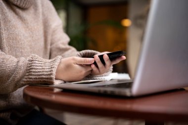 Şehirdeki bir kafede uzaktan çalışan bir kadının akıllı telefonunu açık havada bir masada kullanırken görüntüsü. İnsanlar ve teknoloji kavramları