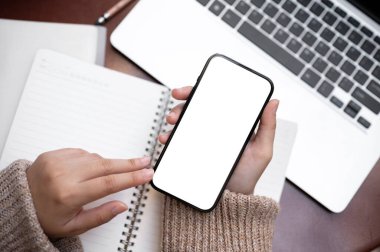 Beyaz ekran akıllı telefonu bir masanın üzerinde tutan, bir kafede uzaktan çalışan bir kadının en iyi görüntüsü. İnsanlar ve teknoloji kavramı