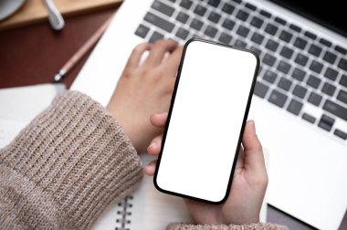 Dizüstü bilgisayarında çalışan ve bir kafede akıllı telefonunu kullanan bir kadının en iyi görüntüsü. Bir kadının elindeki beyaz ekran akıllı telefon modeli..