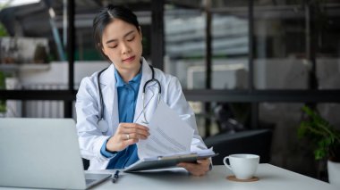 Profesyonel ve düşünceli genç bir Asyalı kadın doktor tıbbi vaka raporlarını kontrol ediyor ve hastanedeki ofisinde çalışıyor..