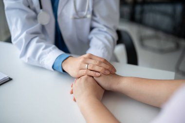Hastanedeki sağlık kontrolü sırasında hastanın ellerini tutan ve güvenini tazeleyen şefkatli ve nazik bir doktorun yakın plan görüntüsü..