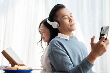 Yakışıklı, Asyalı genç bir adam kız arkadaşıyla evde boş zamanlarının tadını çıkarıyor. Kız arkadaşı kitap okurken kulaklıkla müzik dinliyor..