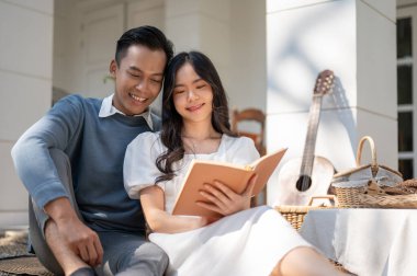 Güneşli bir günde evde piknik yapan, kitap okuyan, eğlenen, konuşmaktan keyif alan sevimli, tatlı, genç Asyalı çift..