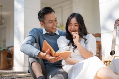 Güneşli bir günde evde piknik yapan, kitap okuyan, eğlenen, konuşmaktan keyif alan sevimli, tatlı, genç Asyalı çift..