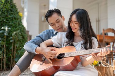 Neşeli ve mutlu genç Asyalı çift evlerinin arka bahçesinde gitar ve piknik yaparken eğleniyor. Bağlanma, aşk, ilişki kavramı