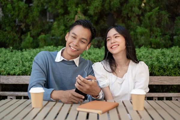 Young Asian couple listening to music together, having fun together in the green park. Couple concept.