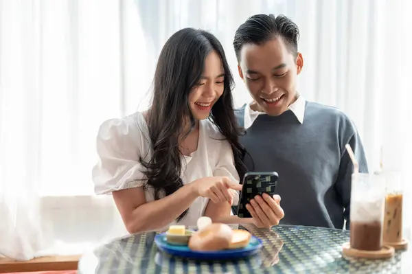 Young Asian couple having a date in a cute cafe, having good time together and playing with smartphone. Couple concept.