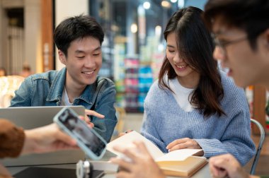 Mutlu bir Asyalı genç adam bir kafede ortak bir proje üzerinde çalışırken arkadaşlarıyla konuşuyor. kolej öğrencisi, arkadaşlık, yaşam tarzı