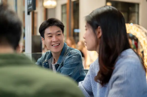 A cheerful young Asian man enjoying talking with his friends while hanging out at a cafe in the city together on the weekend. Friends and lifestyle concepts