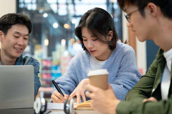 Group of young Asian college students is focusing on working on a co-project or preparing for an exam while sitting in a cafe in the city together. Friendship and lifestyle concepts